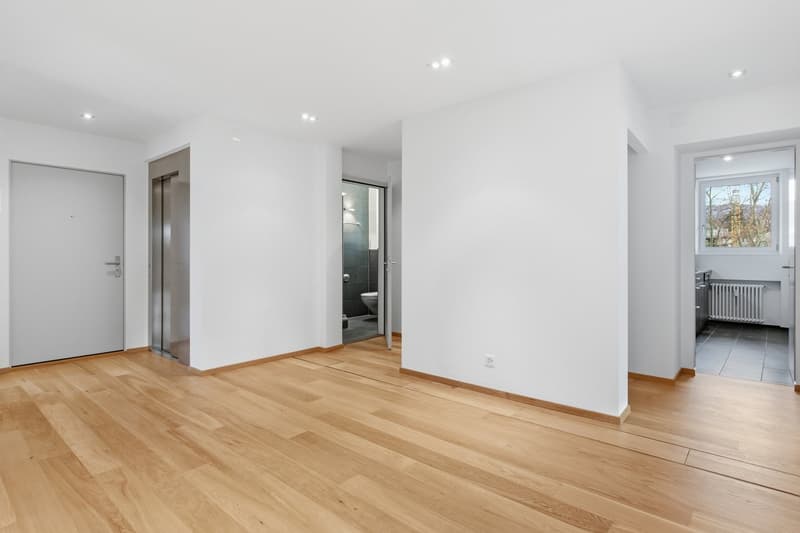 Empty room with white walls, wooden floor, and an elevator on the left side.