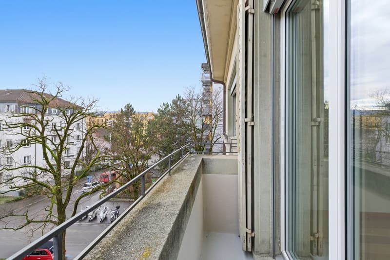 Balcony with metal railing, concrete floor, glass window, view of street and trees