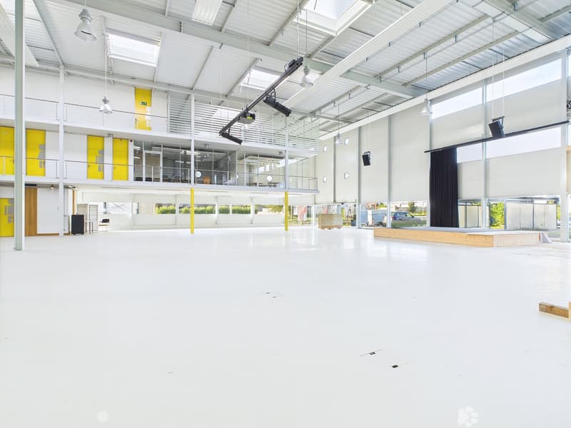 Large open-plan commercial space with high ceilings, exposed beams, and ample natural light from the windows. The space appears to be a studio or event venue with a stage-like platform and lighting equipment installed.