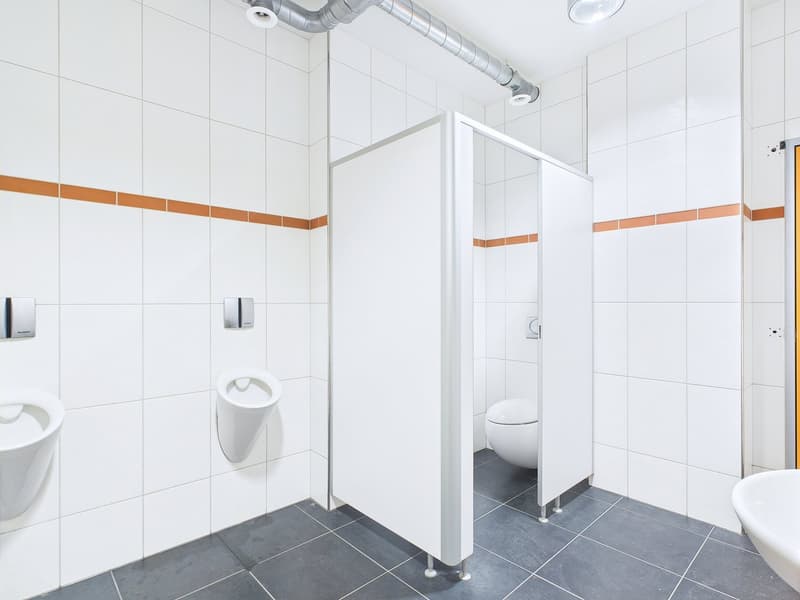 White tiled walls, gray tile floor, toilet, urinal, shower stall with glass door