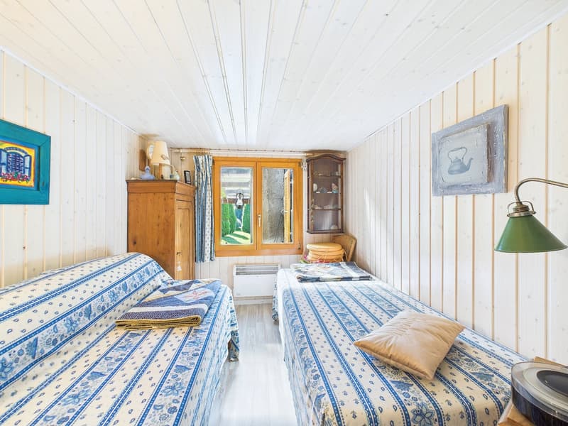 two single beds, wooden cabinets, wooden wall panels, wooden floor, small window, lamps