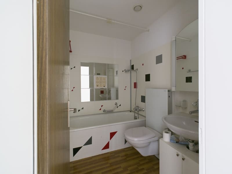 Bathroom with white walls, tiled floor, bathtub, toilet, sink, and mirror. The bathroom has a modern, minimalist design with geometric patterns on the tiles.