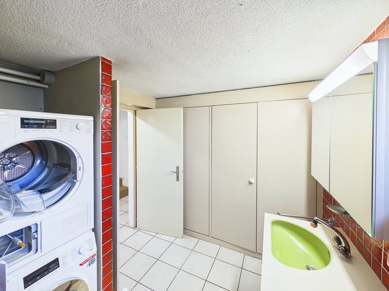 A small room with a washing machine, a sink, and a mirror.