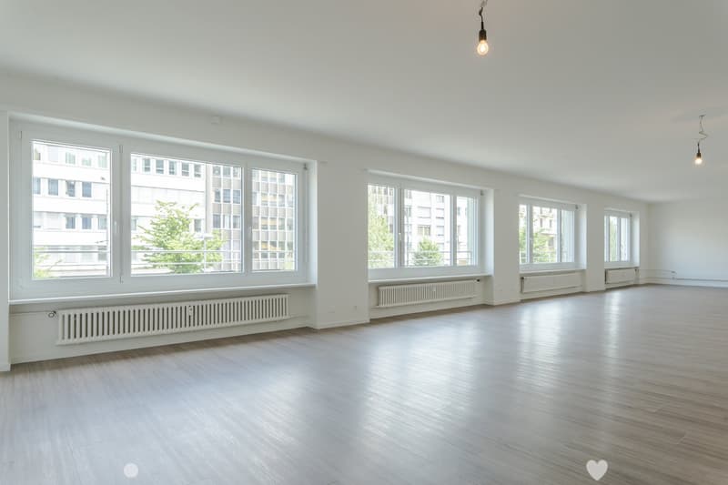 large room, hardwood floors, large windows, white walls, white radiators, ceiling lamps