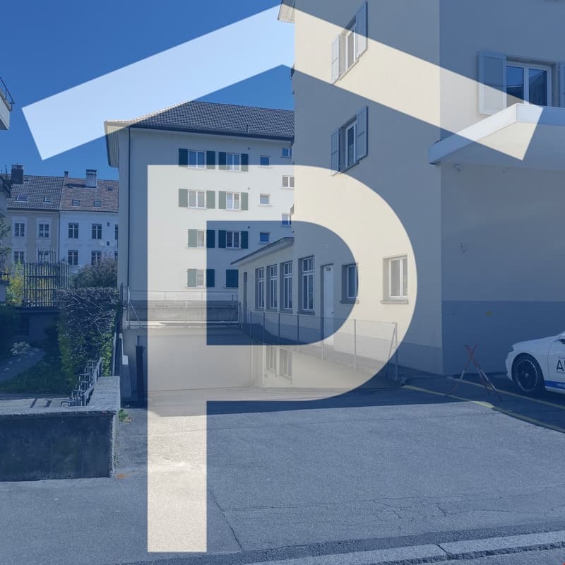 Building with multiple windows, parking area, concrete fence, white car parked