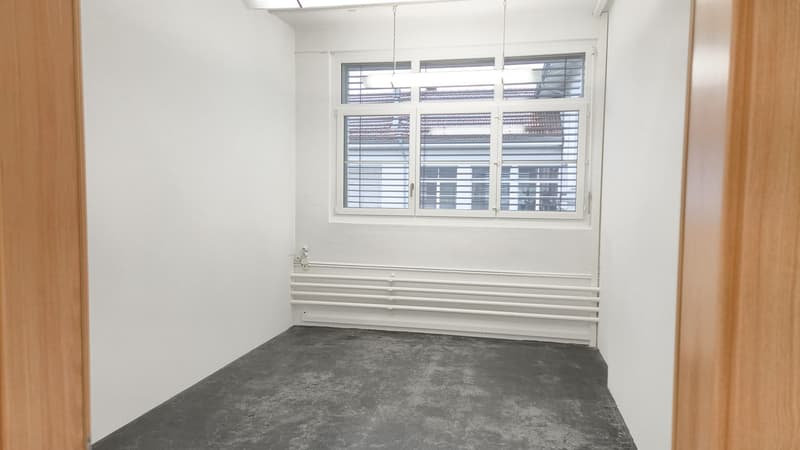 Empty room with white walls, gray floor, radiator, window, and fluorescent lighting