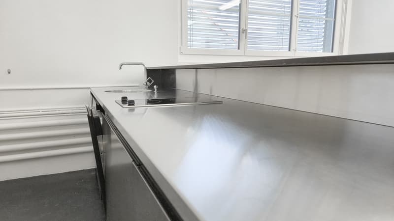Modern kitchen with white walls, stainless steel countertops, an induction hob, and a sink with a faucet. No visible appliances.