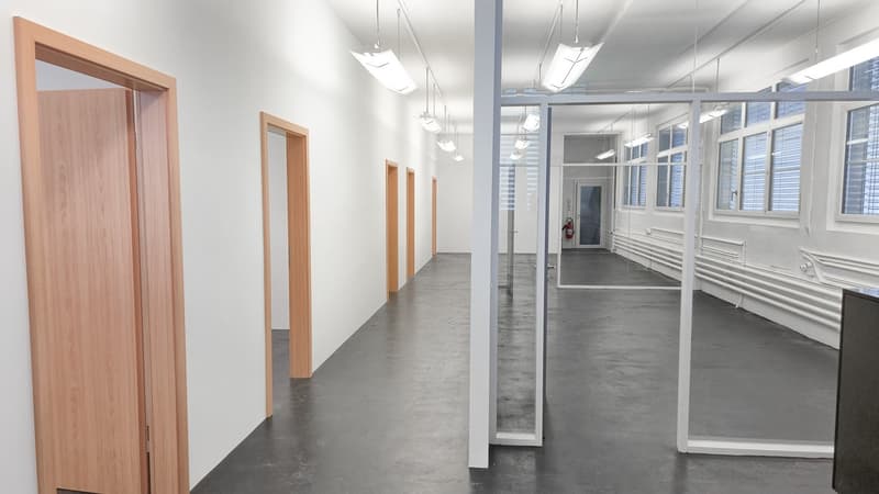 long corridor, white walls, wooden doors, gray flooring, fluorescent lights