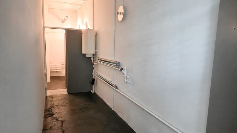 Concrete floor, white walls, heater, door to a room with a small stair, ceiling lamp
