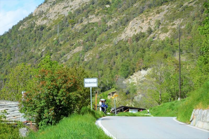 road with a sign Niederried, mountain with green vegetation, small building on the right