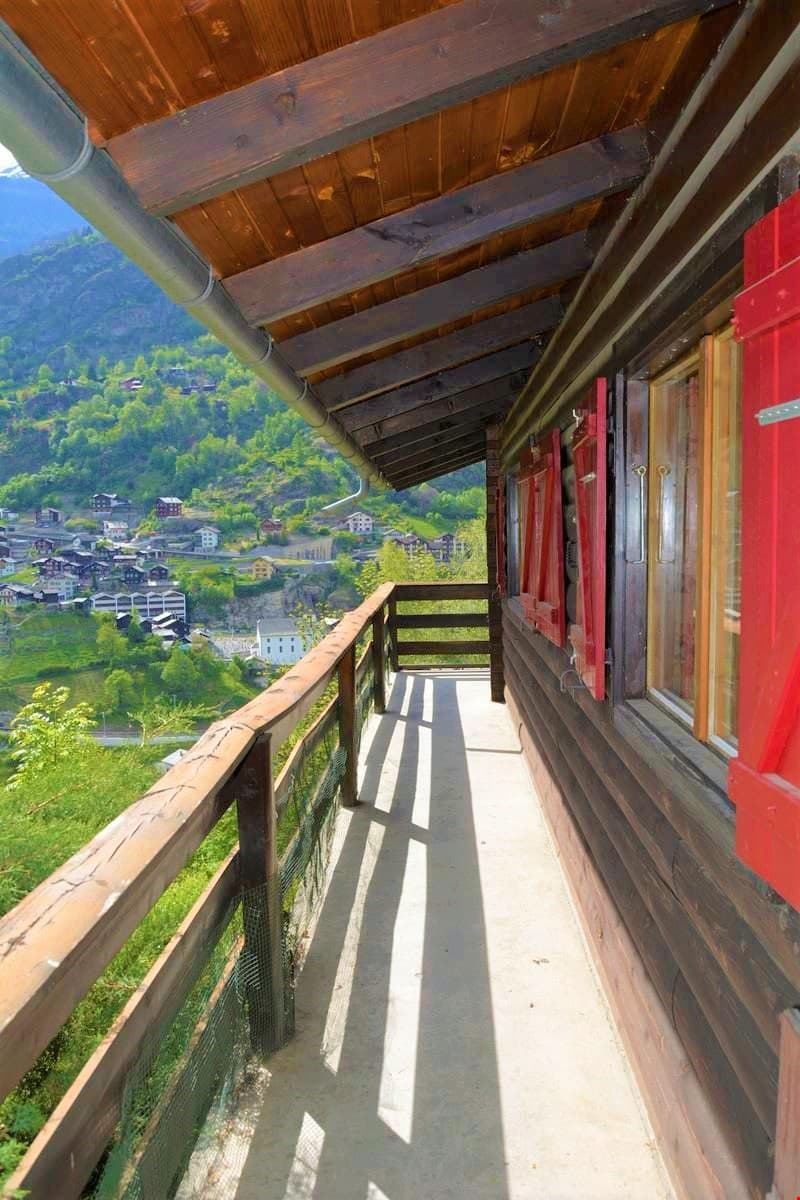 wooden balcony, wooden railing, red shutters, concrete floor, view of mountains and village