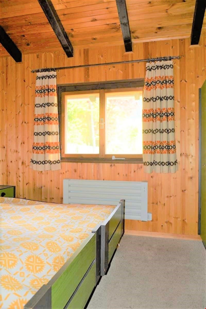 bedroom with two beds, wooden walls, window with curtains, radiator