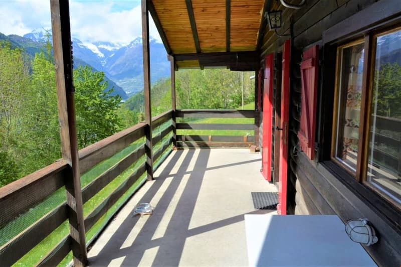 wooden balcony, wooden railing, wooden floor, table, lamp, green grass, trees, mountains