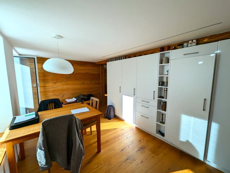Wooden walls, wooden table, white cabinets, refrigerator, desk with computer, and a hanging light fixture