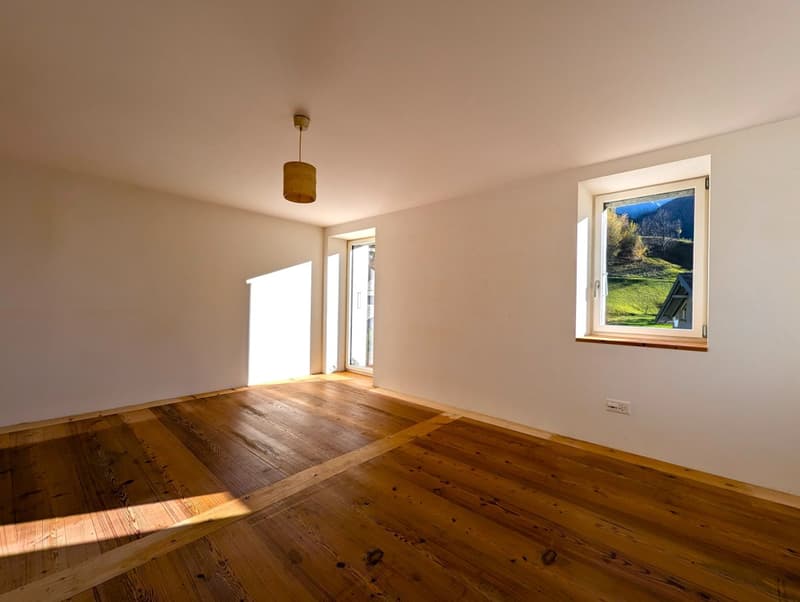 Spacious living room with hardwood floors, large windows providing a scenic view of the surrounding landscape, and a pendant light fixture.