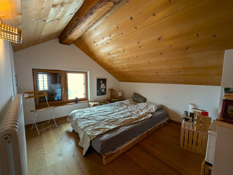 Spacious bedroom with wooden beamed ceiling, large windows, wooden floor, bed, and various furniture pieces