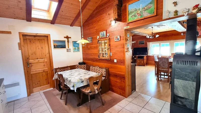 Cozy cabin-style interior with wooden walls and ceiling, a dining table with chairs, a fireplace, and various decorative items and artwork on the walls.