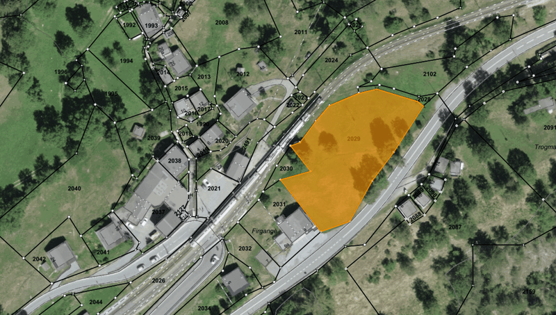 Aerial view of a large, undeveloped land plot with a road running through it. The plot is highlighted in yellow, indicating it is a potential real estate development site.