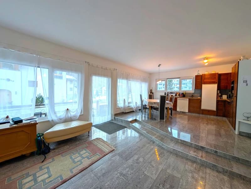 Open layout, large windows, hardwood floors, dining table and chairs, kitchen with cabinets and countertop, white appliances, rug.