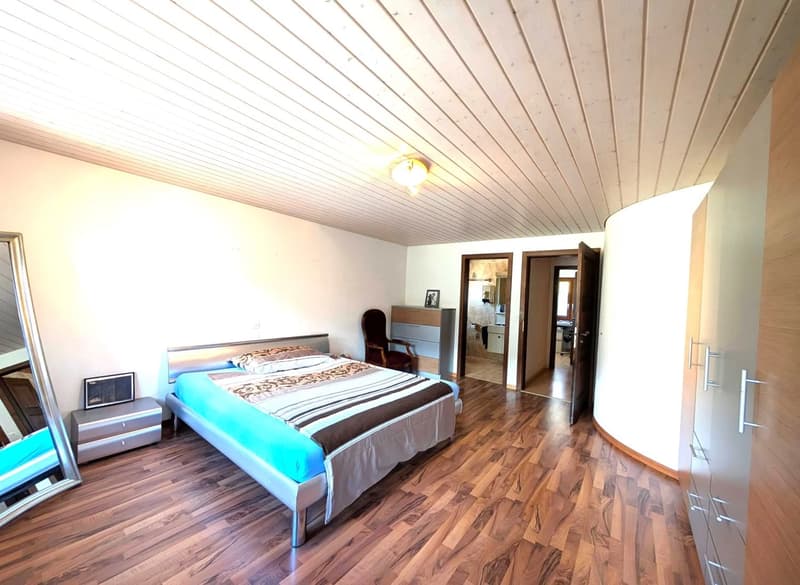 Hardwood floors, white walls, ceiling with wooden panels, bed, side table, armchair, dresser, mirror, open doors