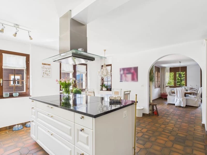 modern design with white cabinetry, granite countertops, large island, gas stove with hood, chandelier lighting, white walls, wooden floors, two windows with white curtains