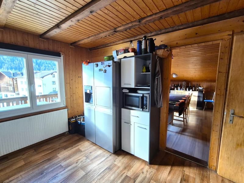 Wooden ceiling with exposed beams, wooden walls, hardwood floor, kitchen appliances including refrigerator and dishwasher, shelving unit, and view of adjacent room through open doorway