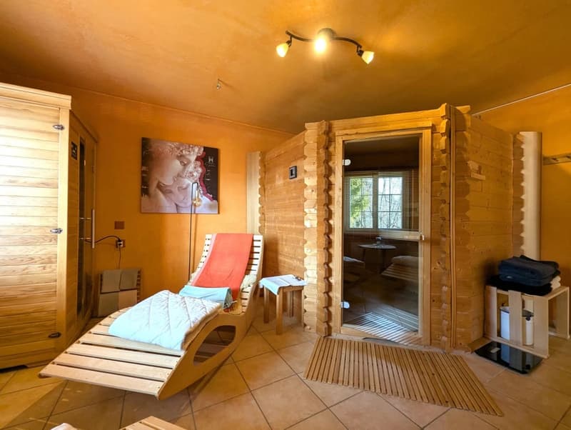 Wooden sauna with lounge chair, small table, towel rack, and artwork.