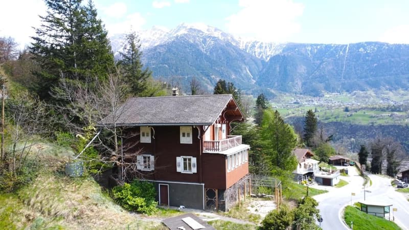 2-story wooden chalet-style house with a balcony, surrounded by pine trees and mountains in the background