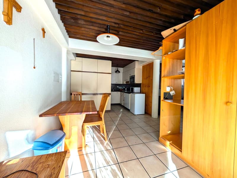 Wooden beamed ceiling, tiled floor, kitchen cabinets, refrigerator, dining table and chairs, shelving unit