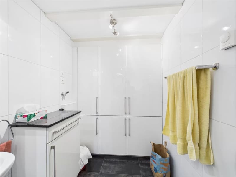 White tiled walls, black tile floor, vanity with sink, large built-in cabinets, yellow towel hanging on the wall