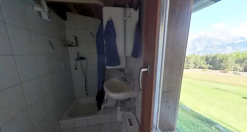 Tiled bathroom with a sink, shower, and hooks for hanging clothes. The bathroom has a window with a view of the outdoor landscape.