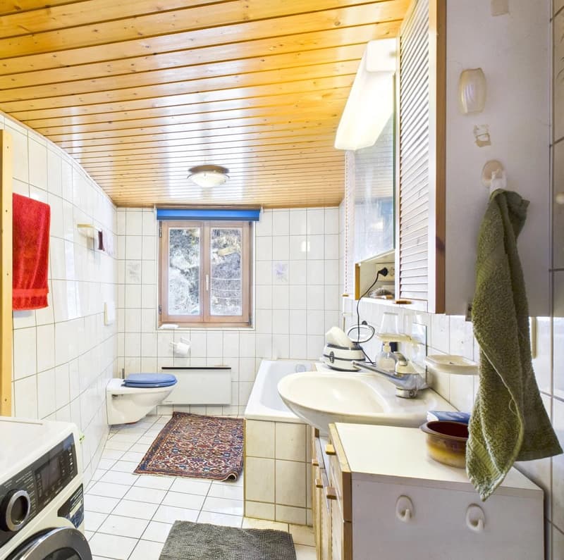 Tiled bathroom with wooden ceiling, toilet, sink, and washing machine