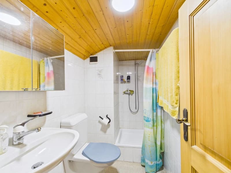 white tiled walls, shower, toilet, sink, mirror, yellow towels