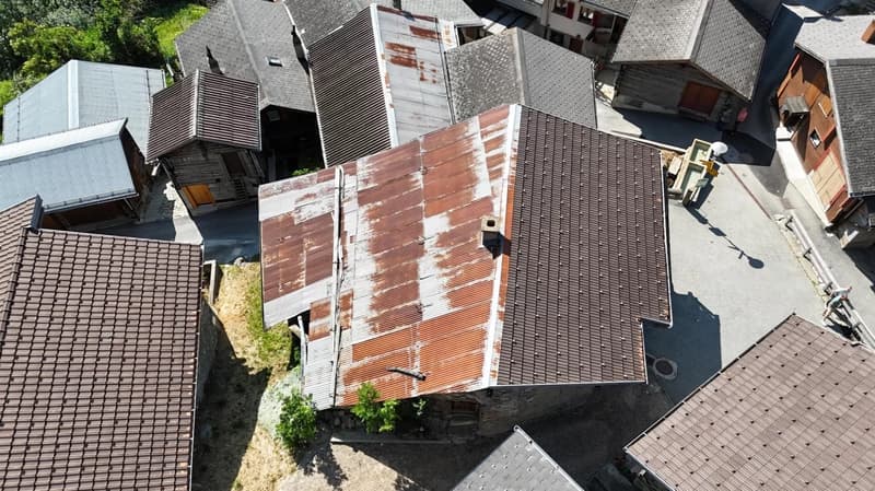 The image shows a bird's eye view of a residential area with multiple buildings. The buildings have a mix of red tile and gray roofs, and some have balconies or terraces visible. The buildings appear to be multi-story structures, and there are trees and g