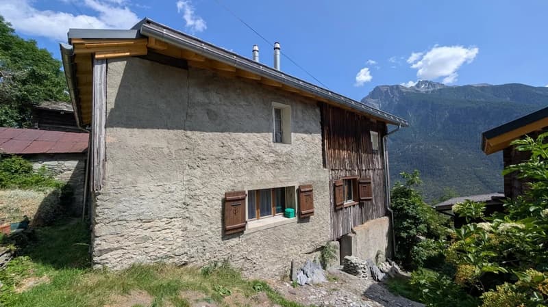 2-story stone and wood house with a slanted roof, wooden shutters, and a balcony overlooking a mountainous landscape