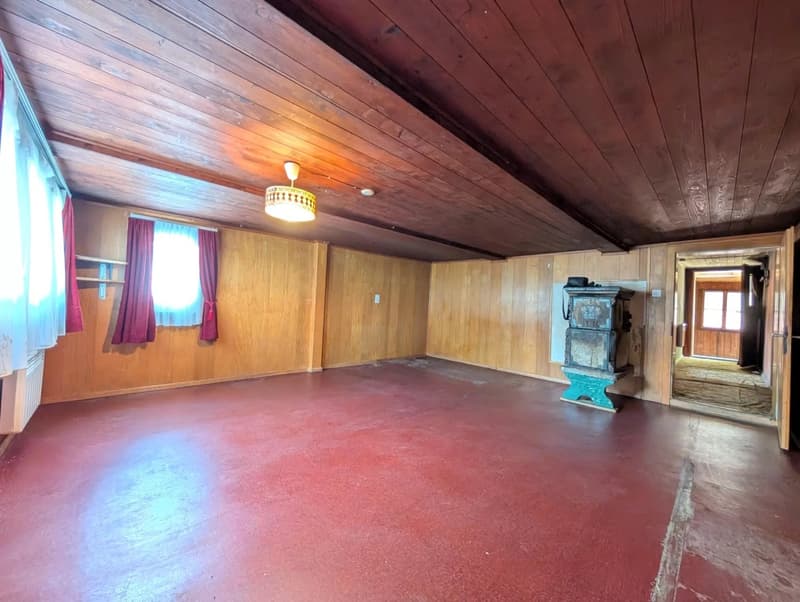 Large open living space with wood paneled walls and ceiling, red concrete floor, and a fireplace in the corner.