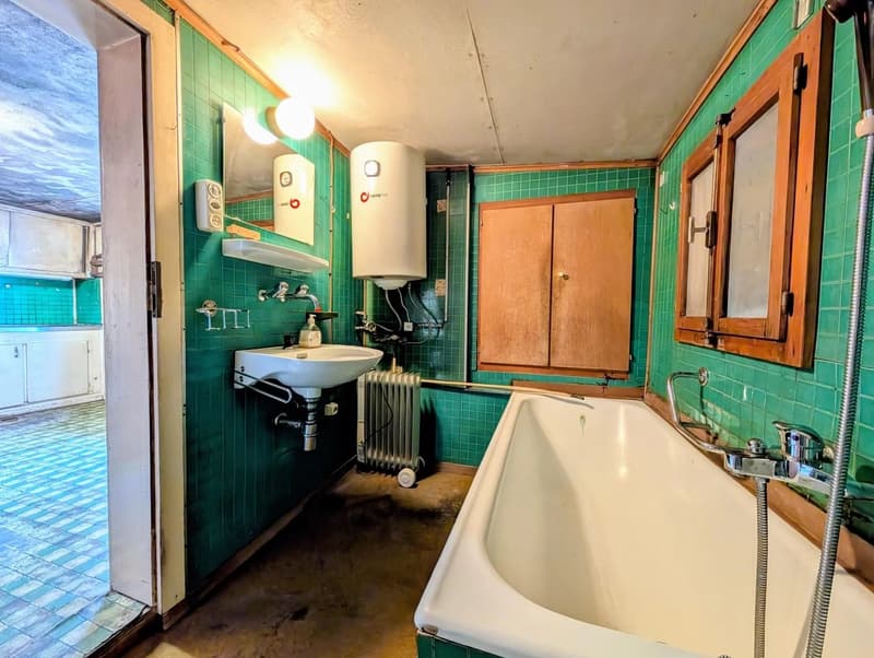 Vintage-style bathroom with green tiled walls, a clawfoot bathtub, a sink with a vanity, and appliances like a water heater and washing machine.
