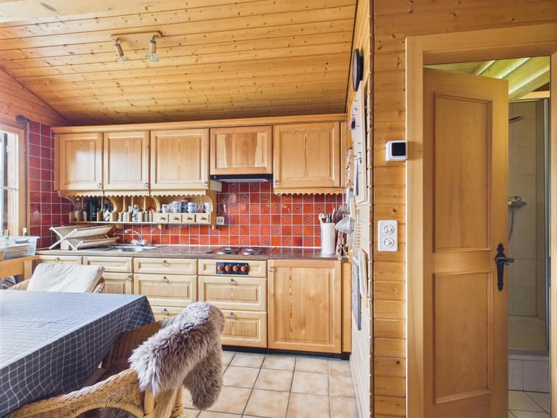 Wooden cabinetry, red tile backsplash, modern sink and stove, overhead lighting, tiled floor