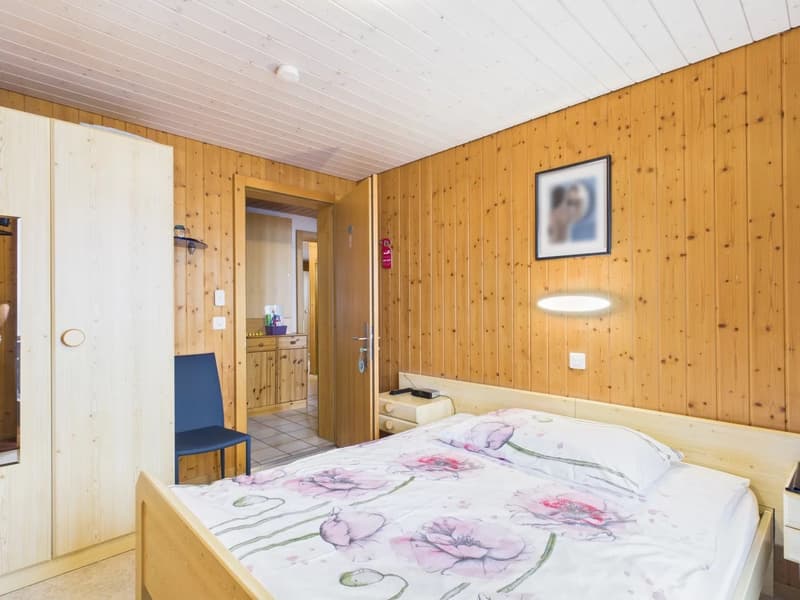 double bed, wooden walls, wooden floor, wooden cabinet, blue chair, desk, lamp