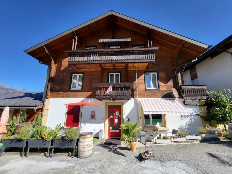 Brown wooden building, 2 balconies, red entrance door, awnings, barrels, plants
