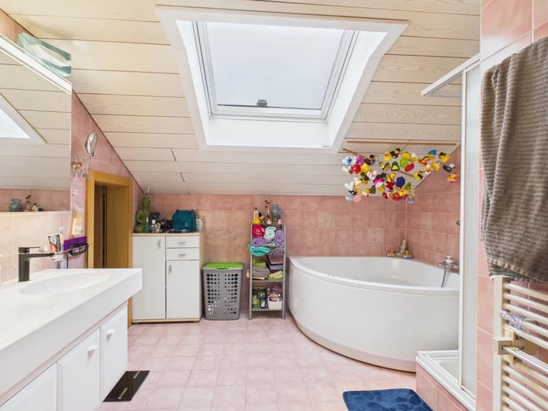 White bathtub, double vanity sink, toilet, radiator, skylight, tiled walls, blue rug