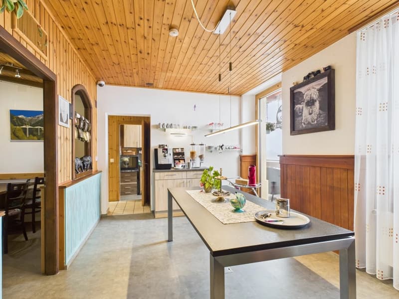 open space with dining table, kitchen area, wooden wall paneling, wooden floor, shelves, hanging lamps, framed picture, large windows