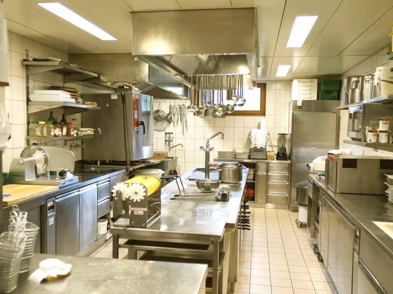 commercial kitchen, large stainless steel counters, gas stove, refrigerator, oven, pots and pans, kitchen utensils