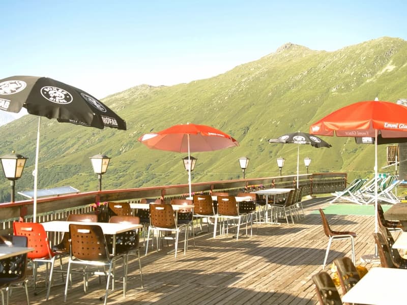 a terrace with tables and chairs, umbrellas, a red fence, and a view of the mountains