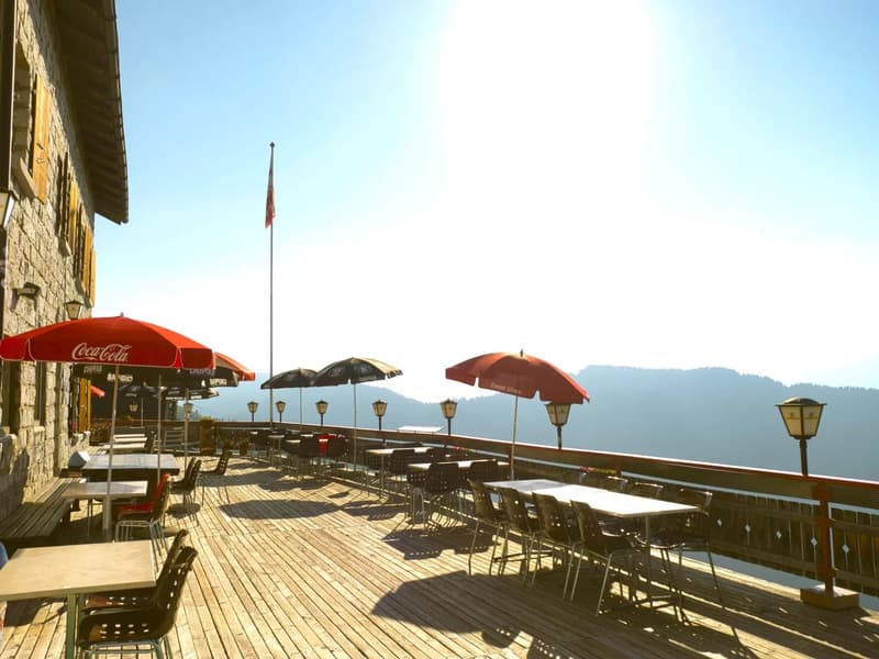 balcony with tables and chairs, red Coca Cola umbrellas, a flag, and scenic view of mountains