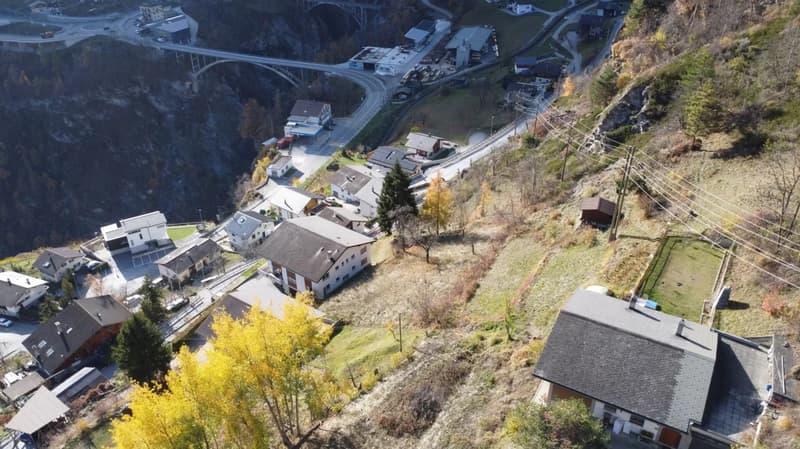 Aerial view of multiple houses on a mountain side, surrounded by trees, a bridge, road and power lines