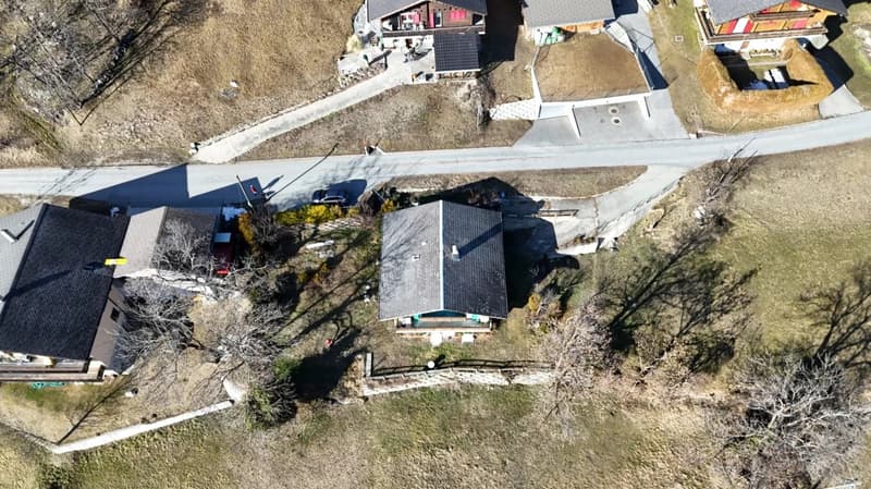 Aerial view of several houses, each with a distinct roof design. Roads leading up to the properties and a car parked near one of the houses. The houses are surrounded by barren fields and sparse vegetation.