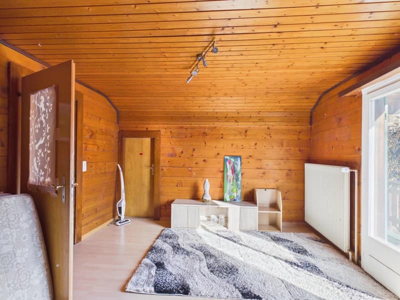 wooden walls, hardwood floors, open door, white radiator, beige rug, side table, vase, open doorway to another room