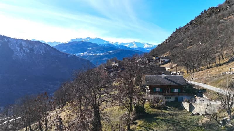 House located on a hillside, surrounded by trees, with mountain views in the background