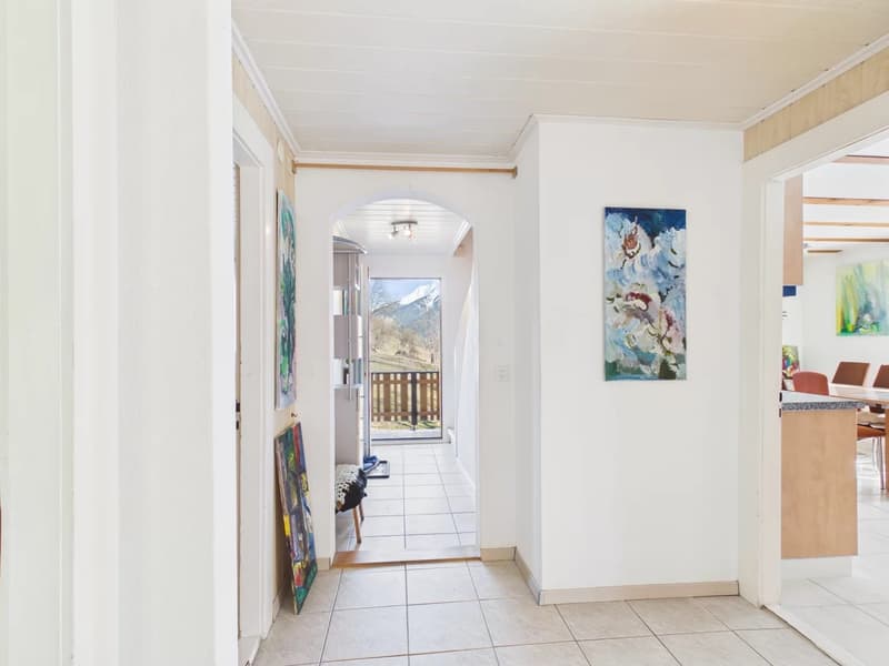 White walls, tile floor, archway leading to terrace, paintings on the wall, small bench